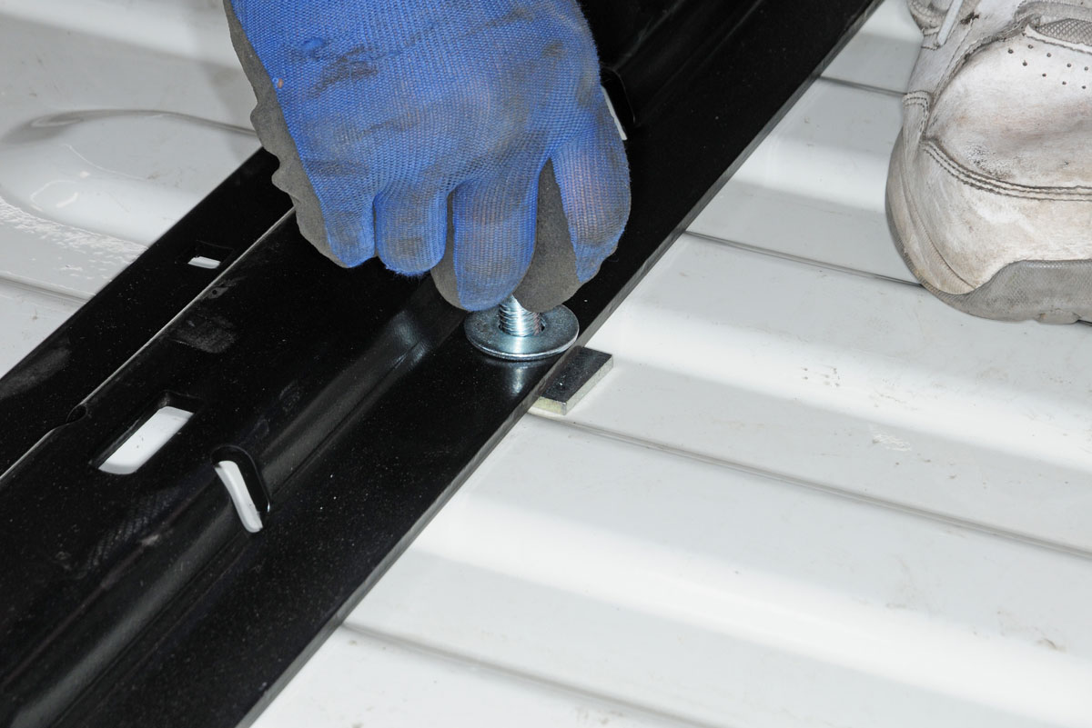 After confirming that the bolt holes are correct, the front rail is bolted into place. Base rail spacers are used to prevent crushing the corrugated truck bed when tightening the bolts.