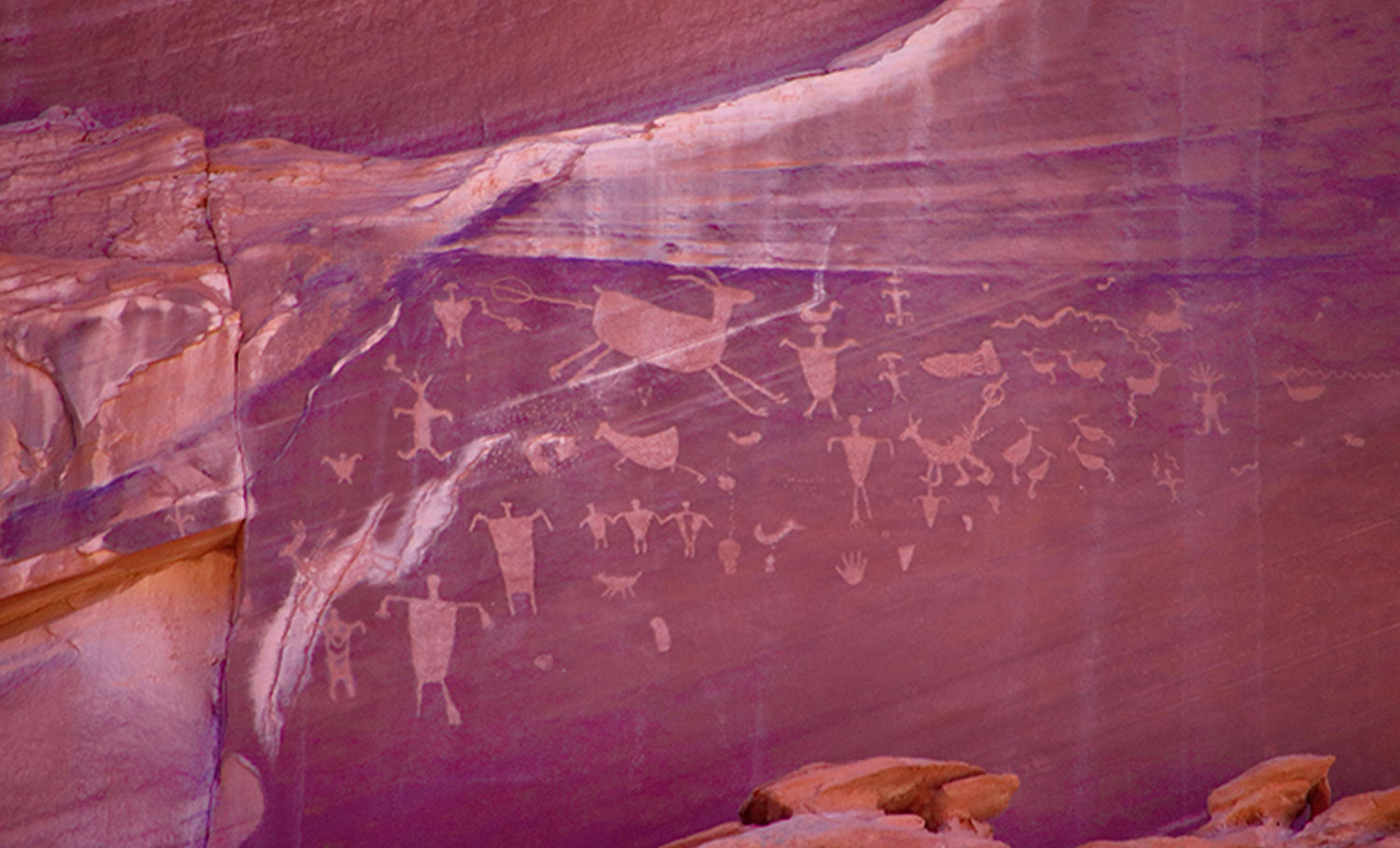a panel of rock located on a canyon wall, showing animal and human figures and handprints