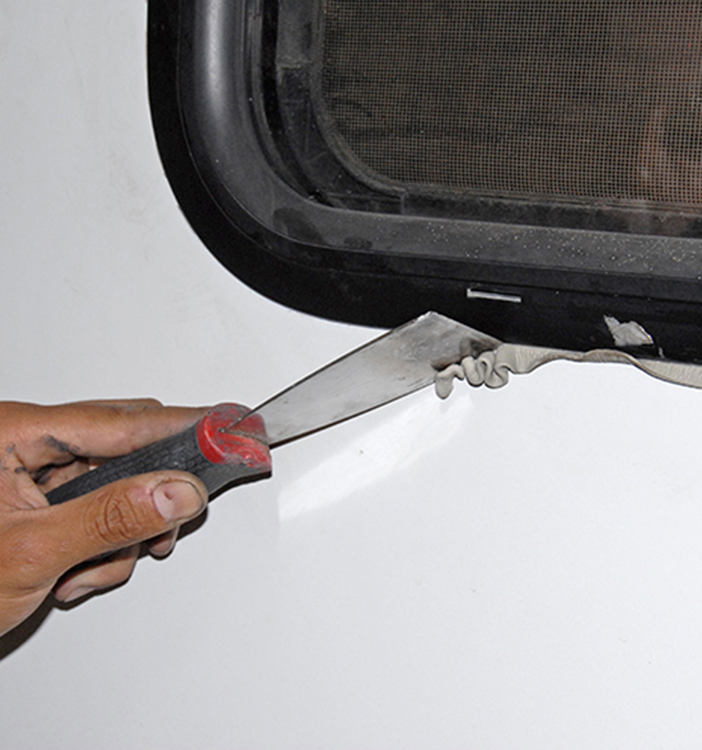 Once the window is screwed back into place, a putty knife is used to remove the excess putty from the exterior wall