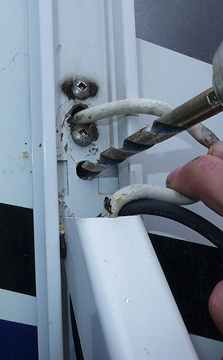 A 7/16-inch hole is drilled through the hardware just below the existing cable into the cupboard where the switch assembly is mounted