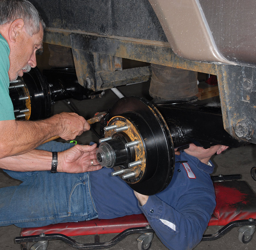 two men working on the wheel area of an RV