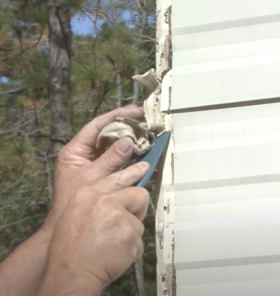 plastic putty knife being used to remove old caulking