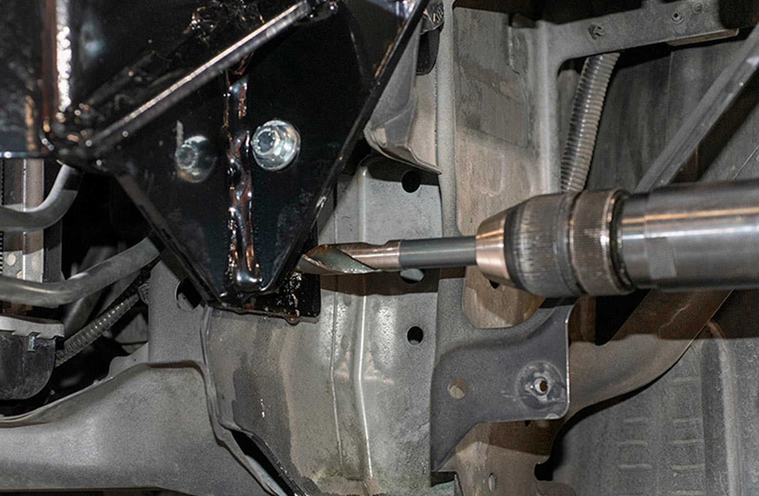 mechanic uses a drill to punch a hole through the Honda’s unibody frame on each side of the baseplate mounting brackets to insert a ½-inch bolt