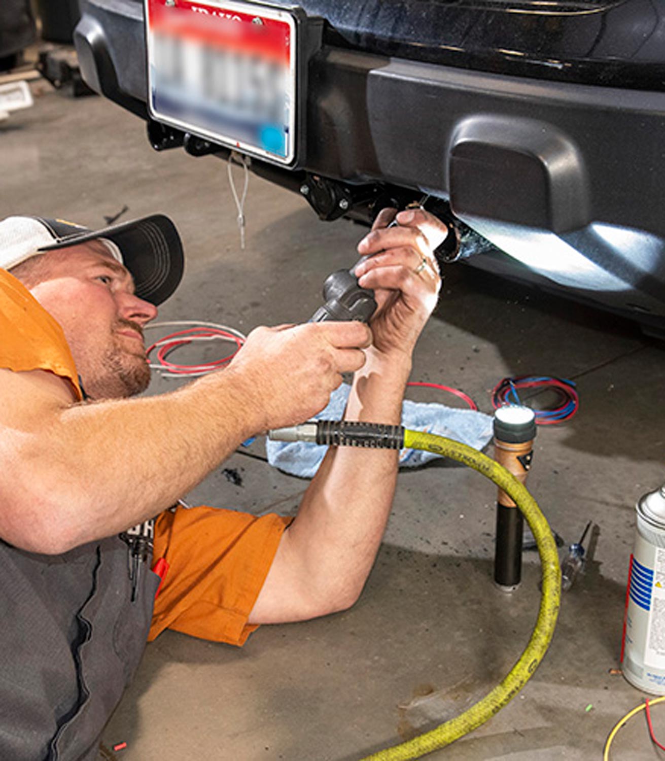 mechanic lays on the garage floor, trimming the plastic bumper/facia so it matches the contours of the new baseplate and connections