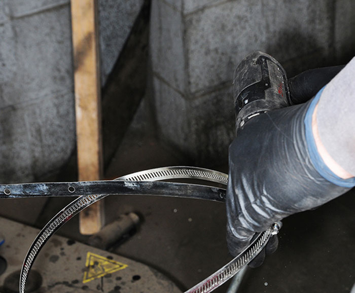 A large metal band that looks like a gigantic hose clamp is unwound using a screw gun so it can be fitted on to the wheel