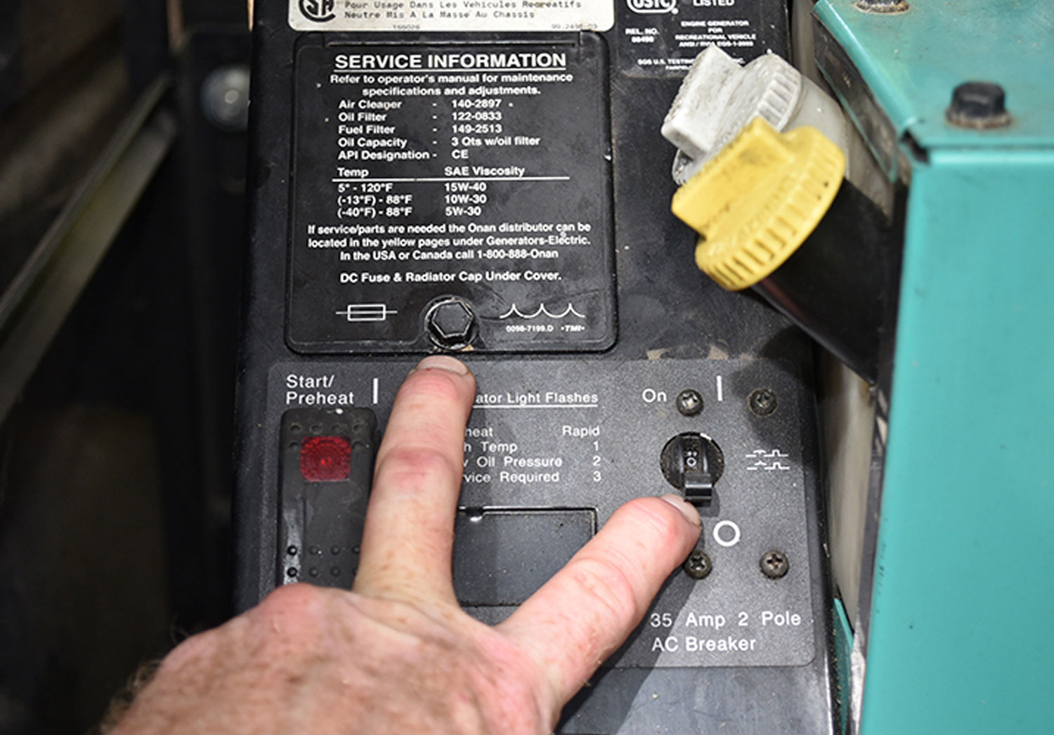mechanics fingers point to the “Off” switch for the generator and the oil fill point and radiator fill point
