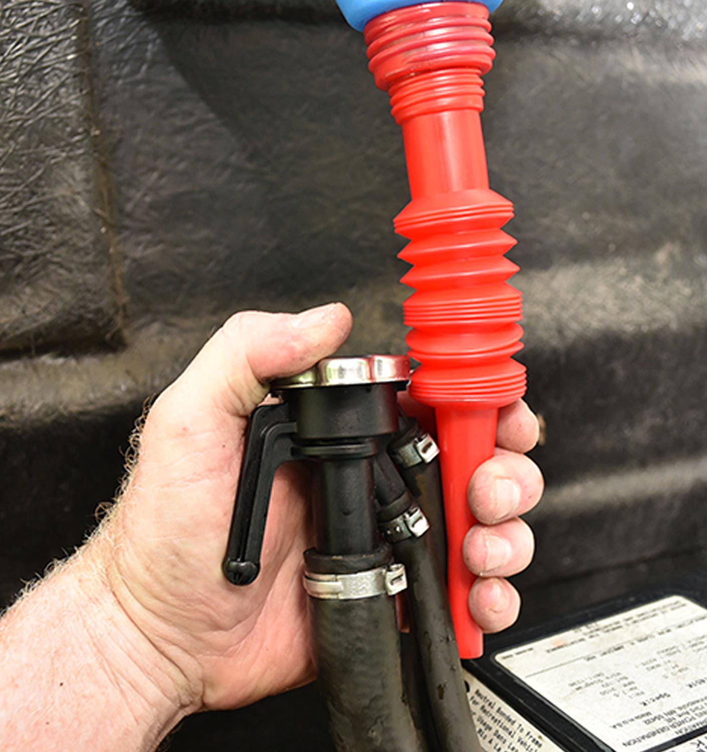mechanic holds the radiator fill hose and funnel side by side in preparation for refilling the radiator with coolant
