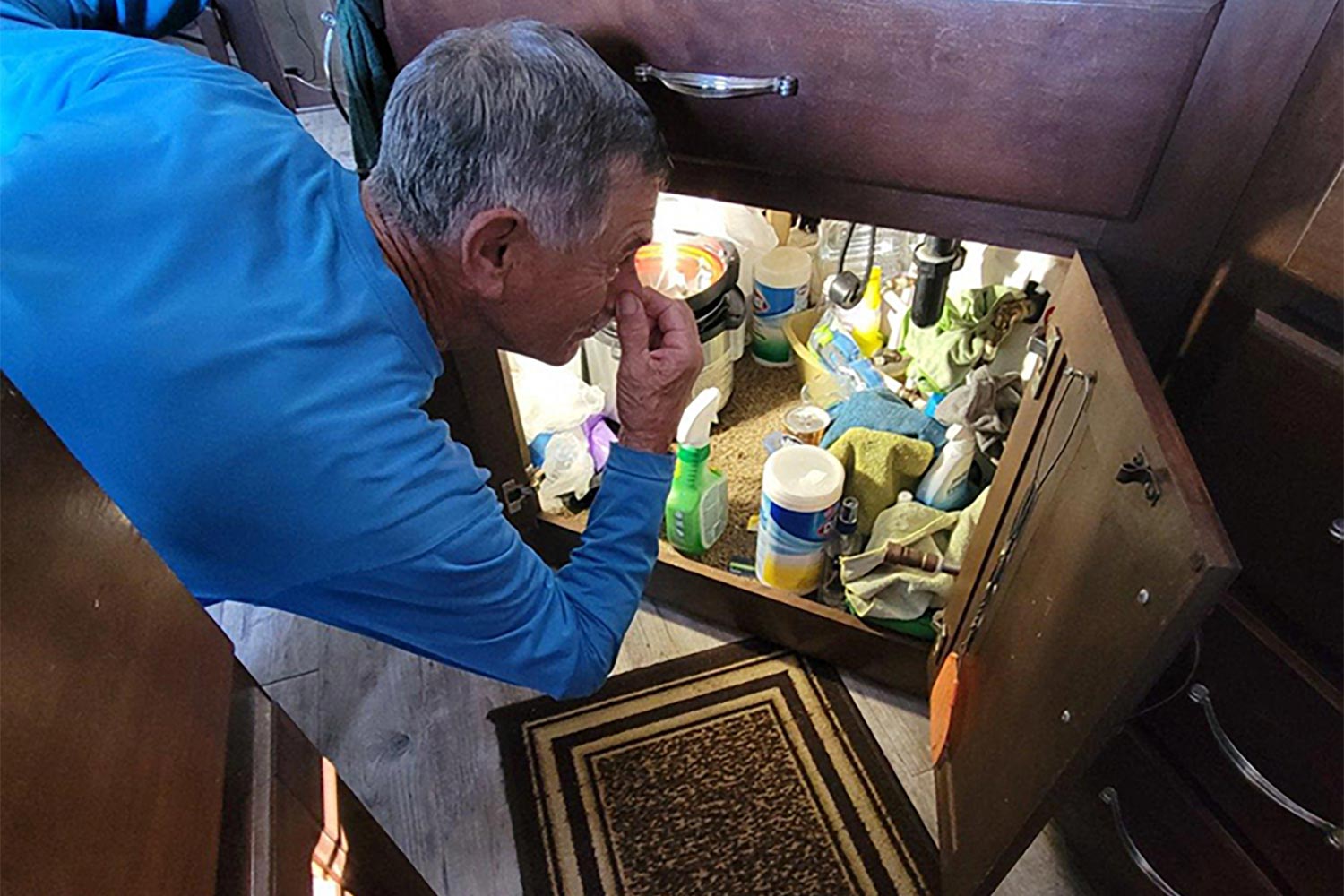 Man opening cabinet underneath RV sink and plugging nose