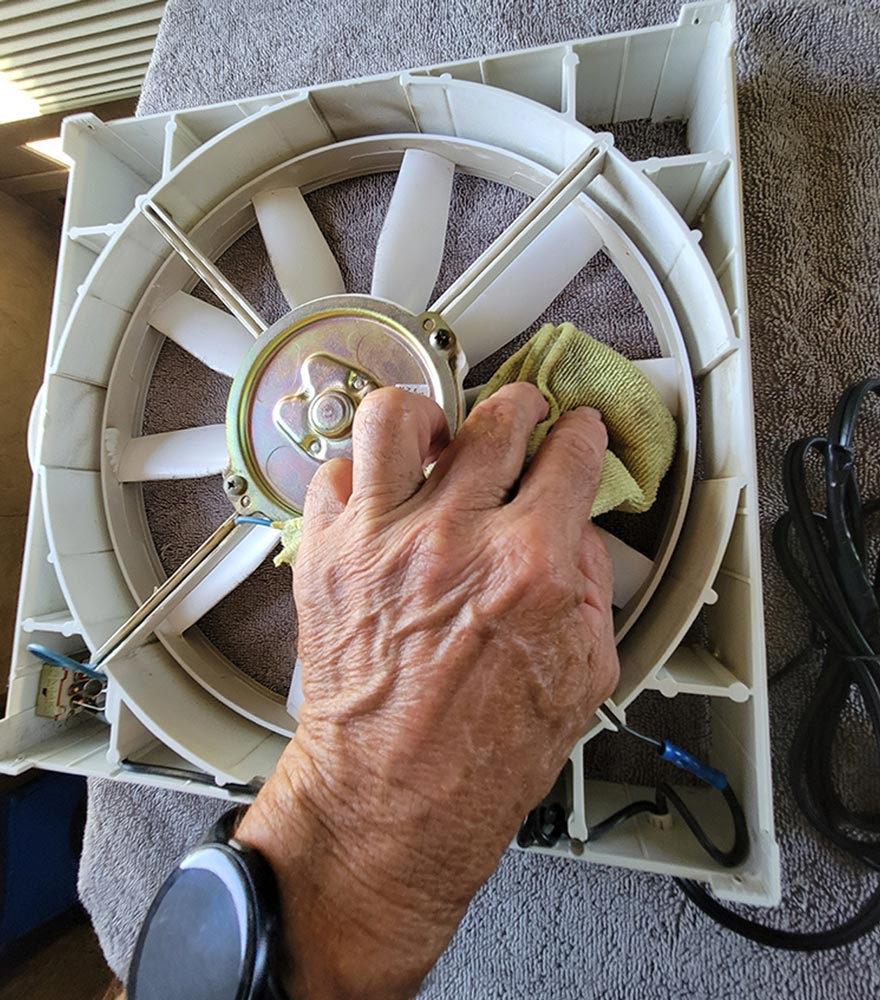 a hand uses a microfiber cloth to clean the exposed blades of the fan