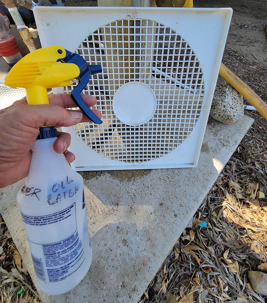 a hand holds a spray bottle in preparation to clean the fans blade protecting cover