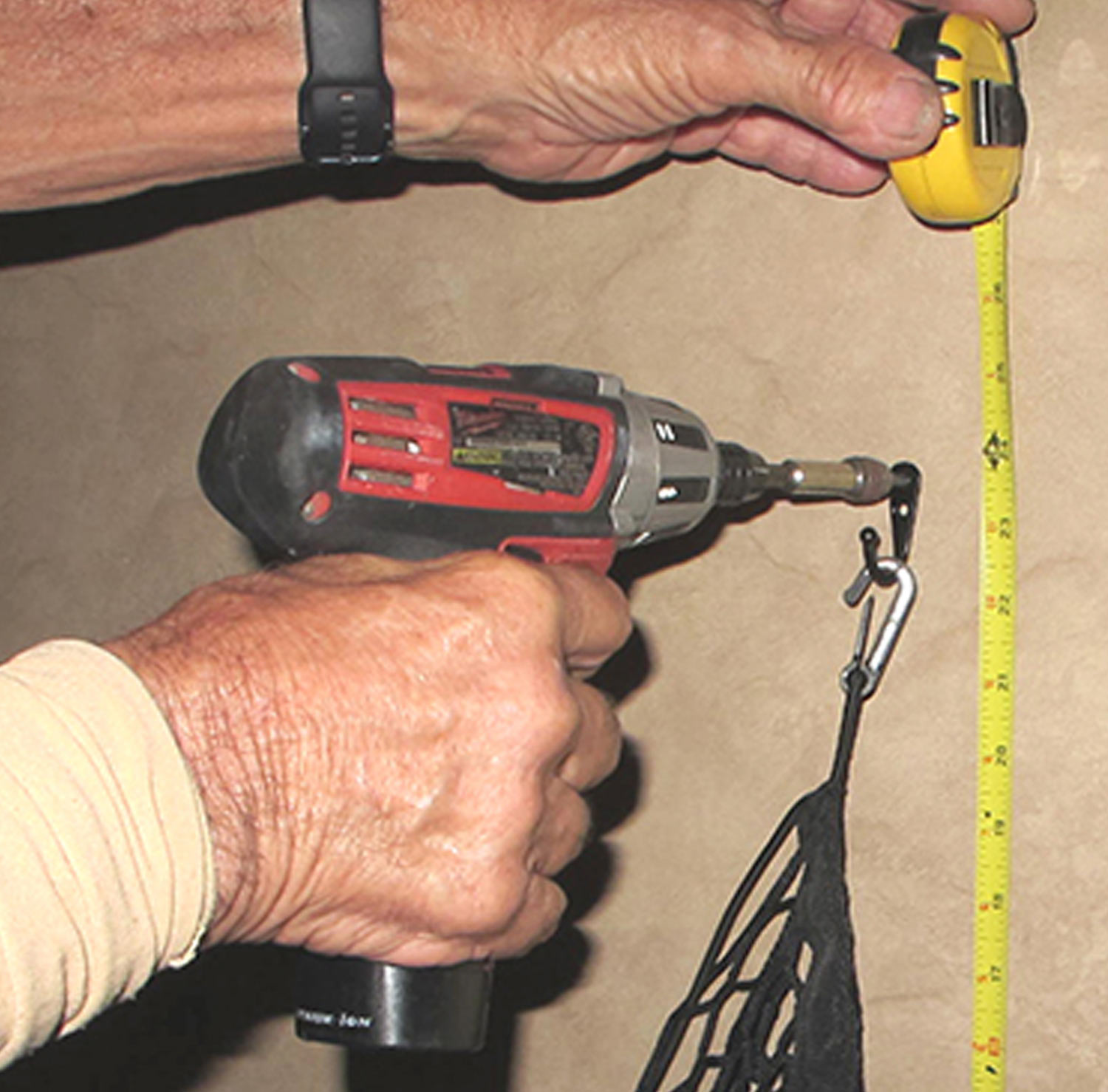 using a tape measure from the ground up, the RV technician drills a hole to attach the first hook to the wall