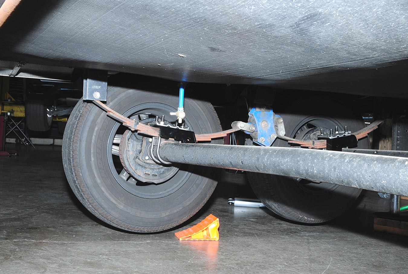 inner view of the underside of the RV showing the springs attached to the axle with tie plates, the shackles welded to the frame and the equalizer mounted in the center