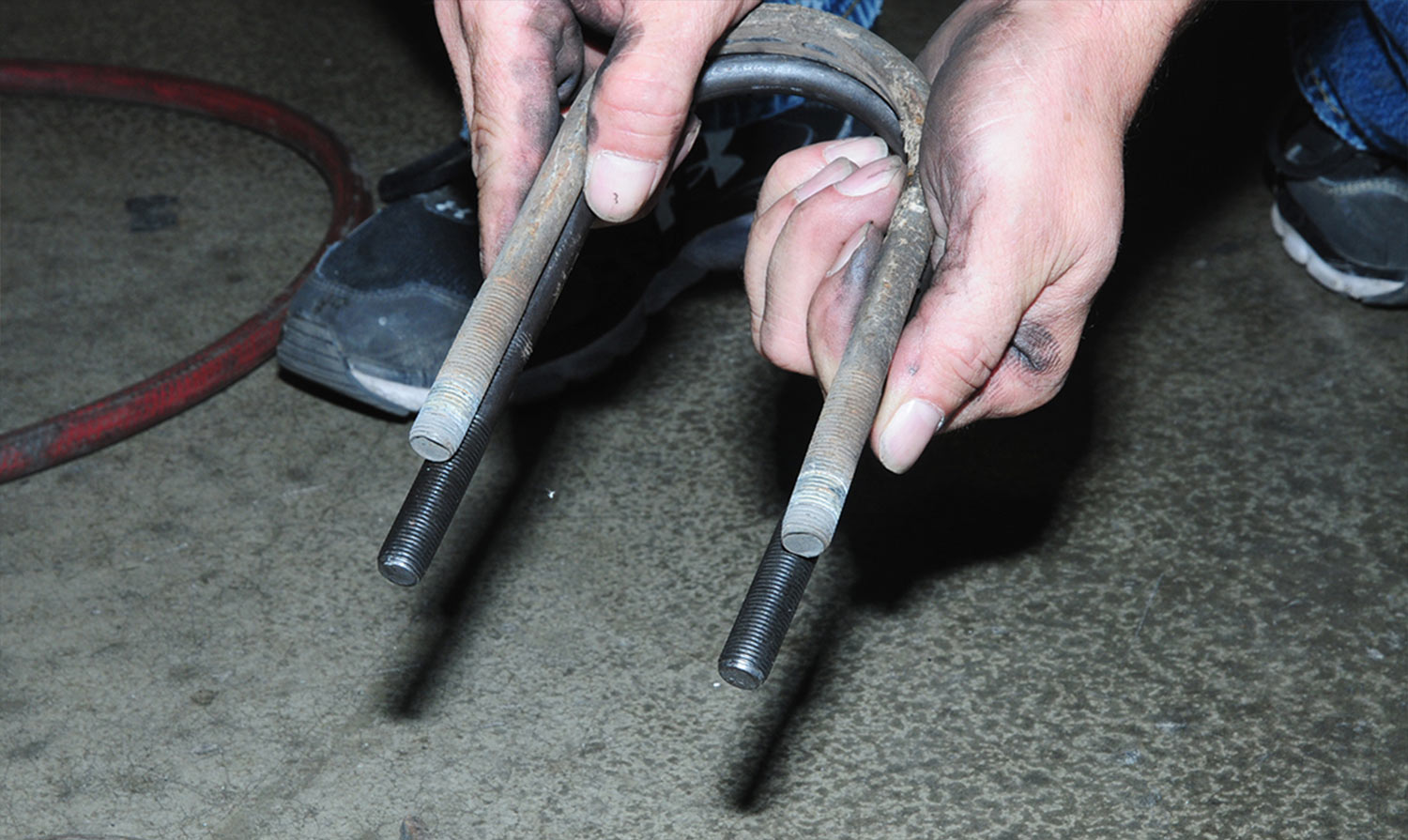 mechanic holds the old and new U-bolts on top of each other to compare