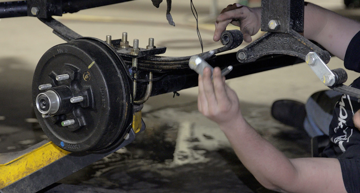 working under an RV, the mechanic removes a stock shackle bracket