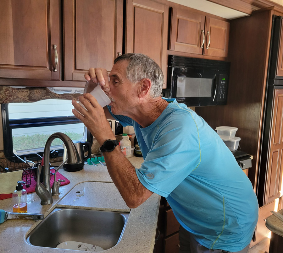 man drinking a glass of water above the sink while holding his nose