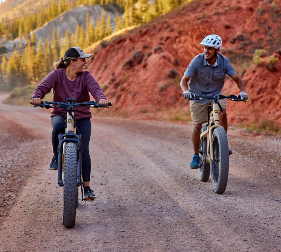 two people riding electric bicycles on a dirt road