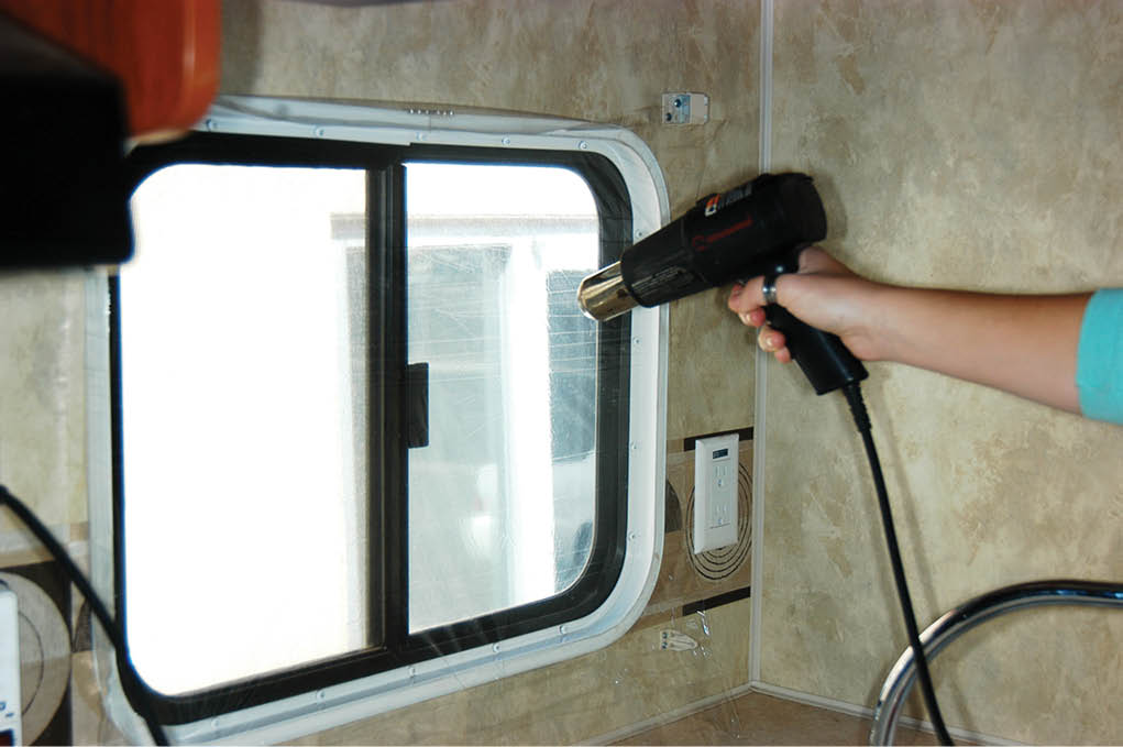 Person adhering vapor barrier to window with heatgun