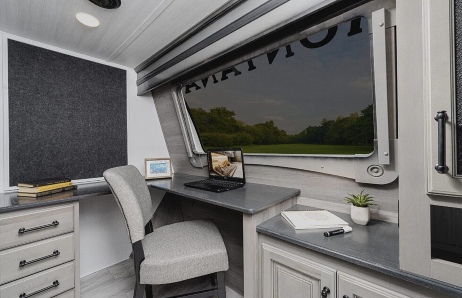 a home office area in an RV, including a desk, a large window and drawers