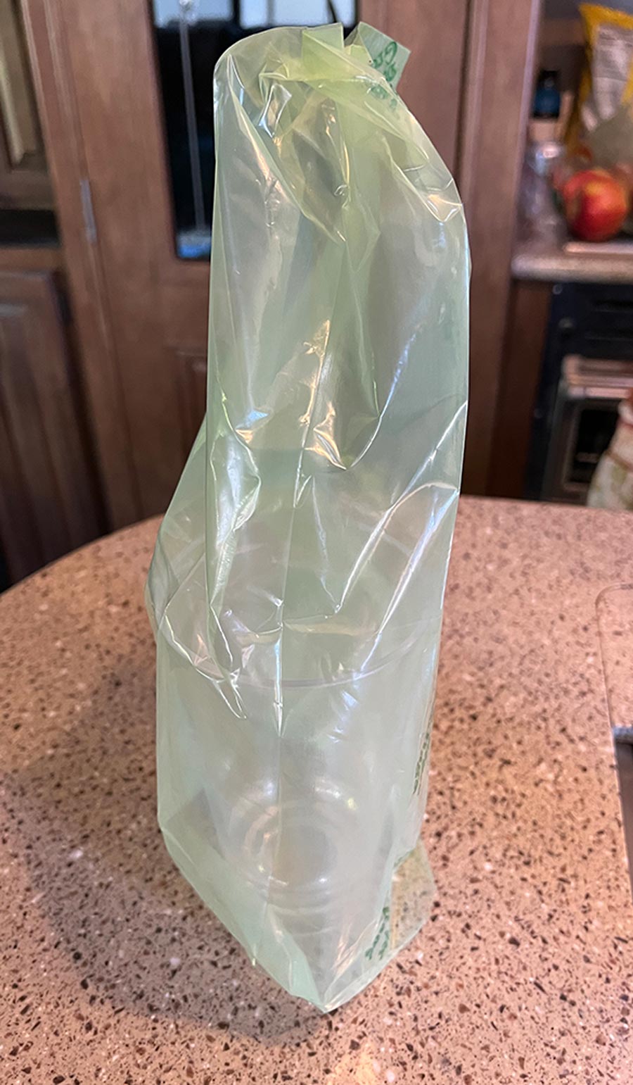 a green bag is emptied out, washed, and placed over a large cup upside down to dry for future usage