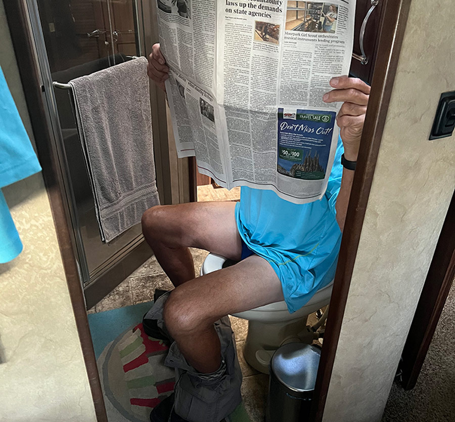 man sitting on the toilet reading a newspaper