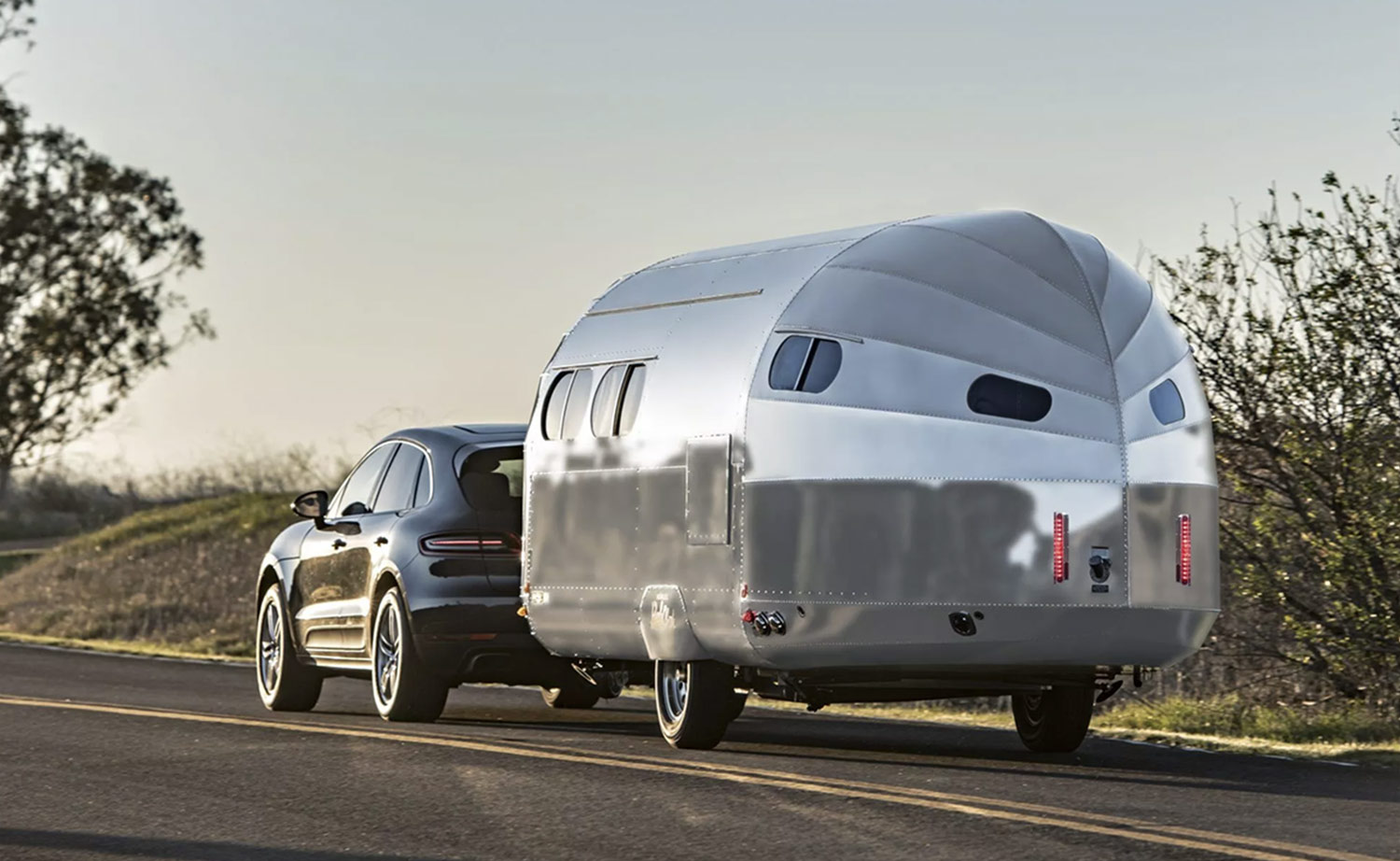 three quarter rear view of the Bowlus Heritage Edition travel trailer hitched to an SUV riding down a road