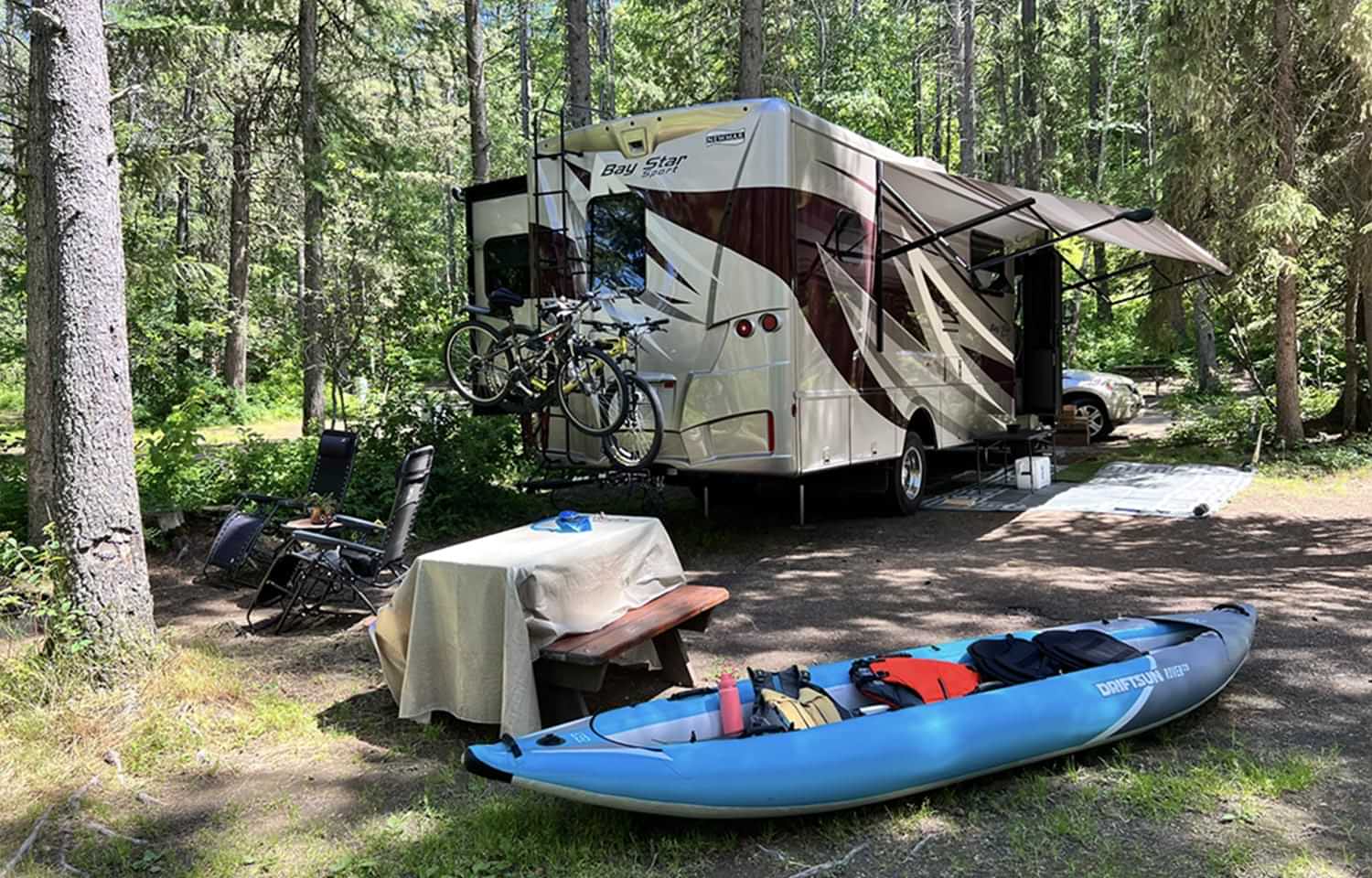 an RV, kayak and small table set up at a camping site