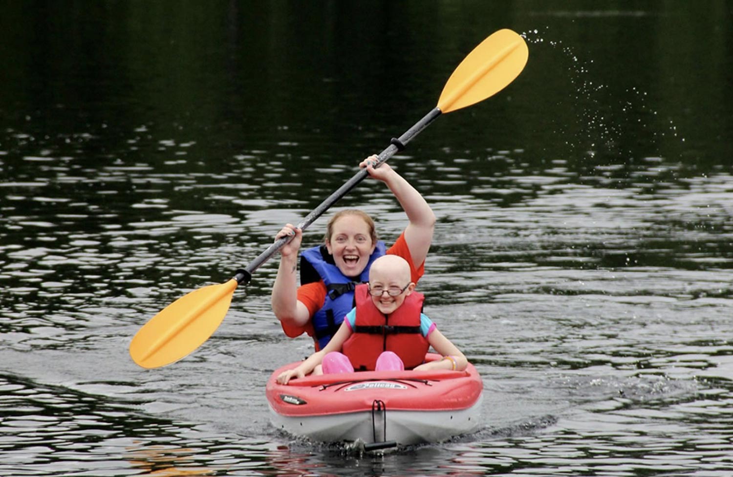 a young girl and a woman smile while paddling in a kayak on a lake