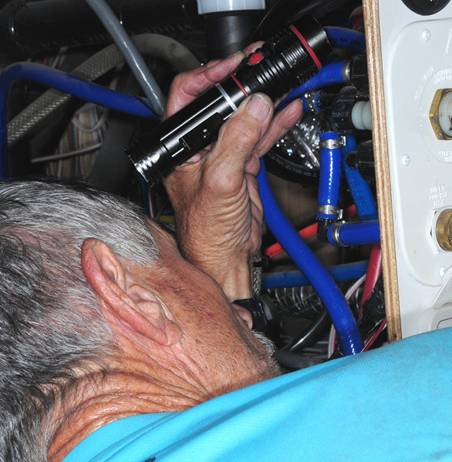 man using a flashlight to look near the plumbing of his trailer