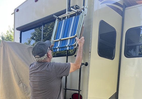 man hanging chair on ladder on the back of an RV