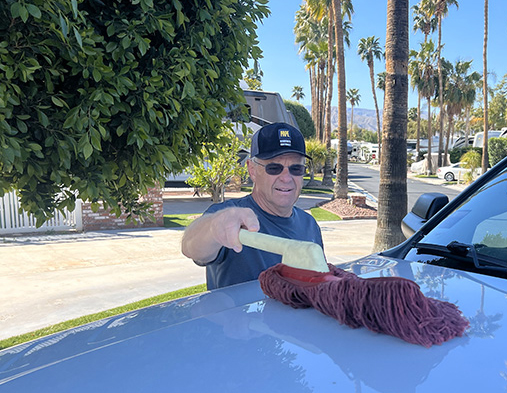 man dusting hood of truck