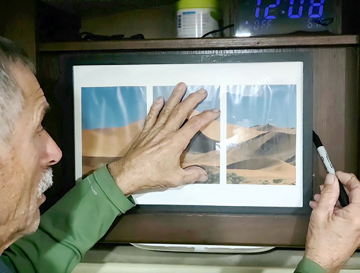 Close-up photograph perspective of Bill Gehr finding “secret” unused space in an RV with a black Sharpie pen by measuring/opening up a bedroom wall area through adding a picture-frame “door” in order to allow capacity for storing extra clothing, sheets and towels.