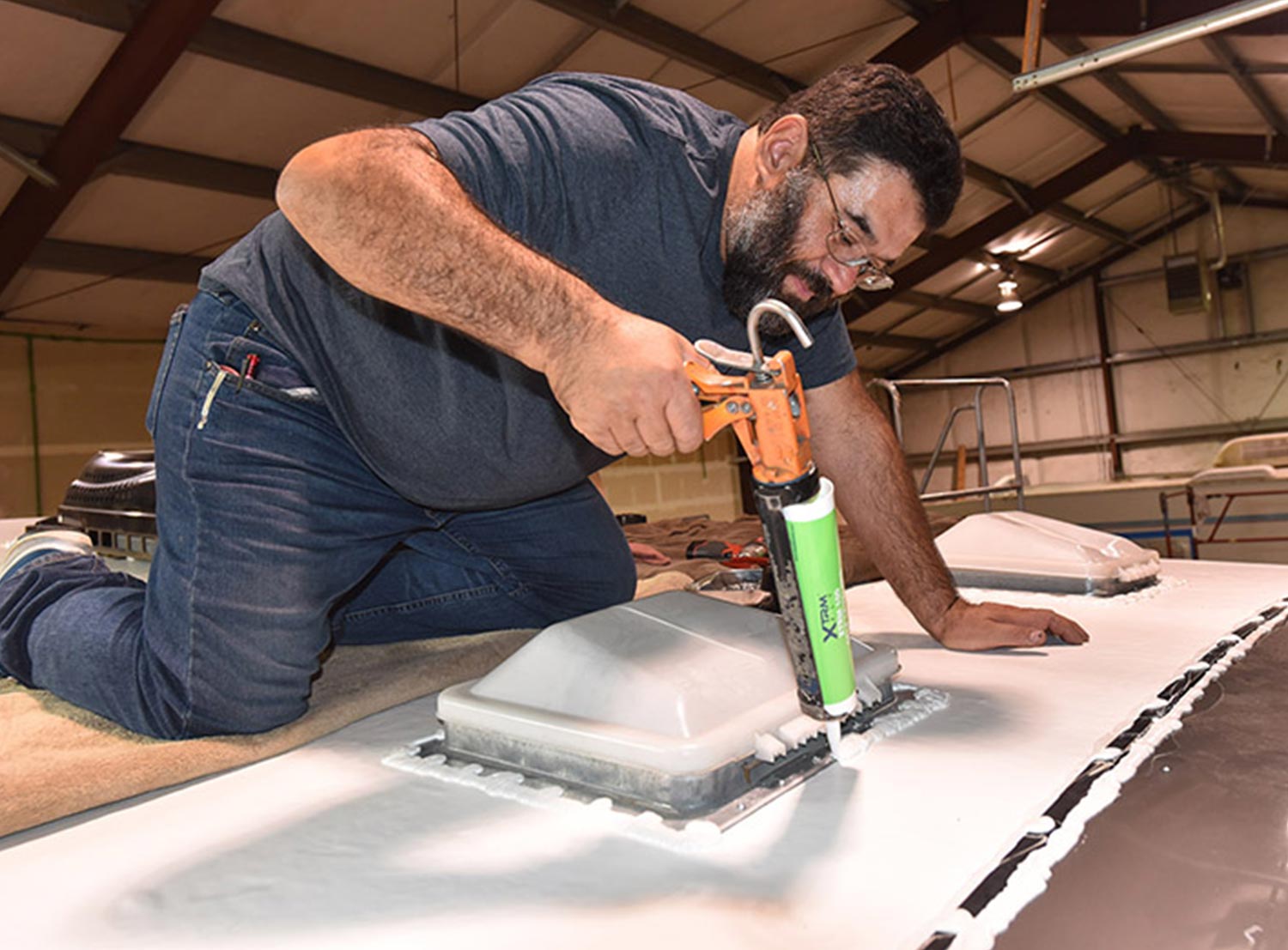 Carrier RV’s Tony Salazar kneeling atop an RV and using a sealant gun on a trailer roof vent