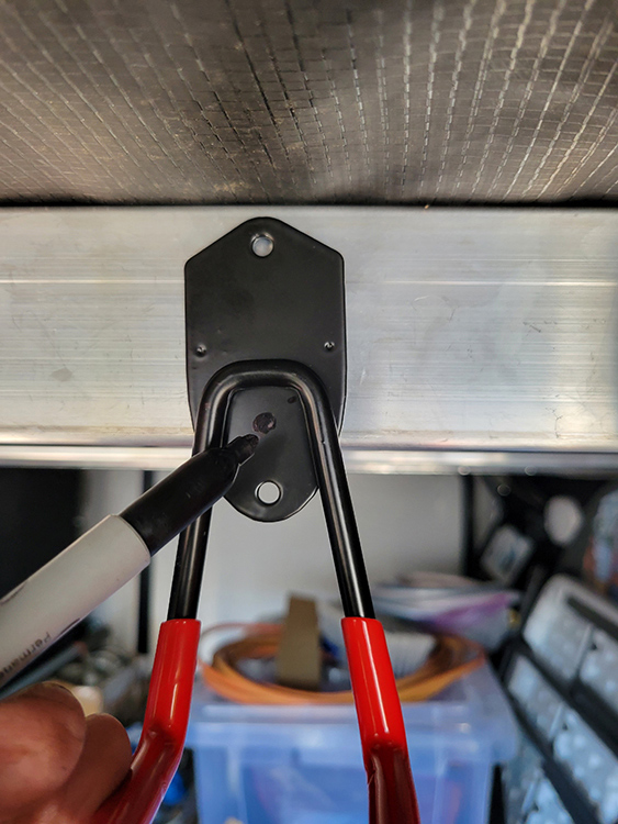 In order to securely mount the hooks with two screws that could be spaced properly on the 2-inch rafters, I drilled an additional hole through each hook base. Once the extra hole was drilled, the location for one of screws was marked on the rafter for drilling a pilot hole.
