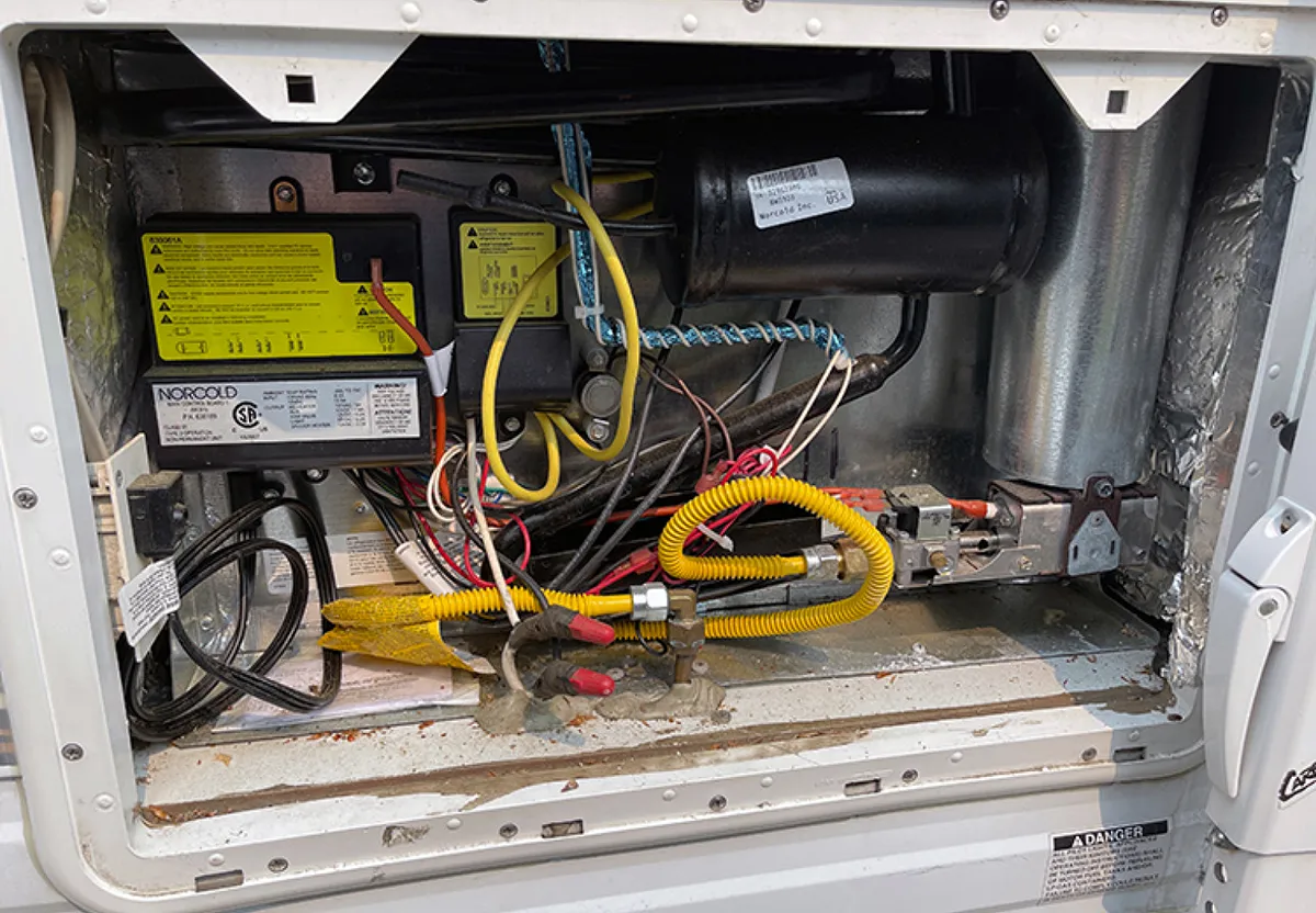 Opening the back vent door of this Norcold Polar 7 refrigerator shows some dirt and dust, but overall it’s pretty clean. The chimney tube is on the right, attached to the burner on the lower right.