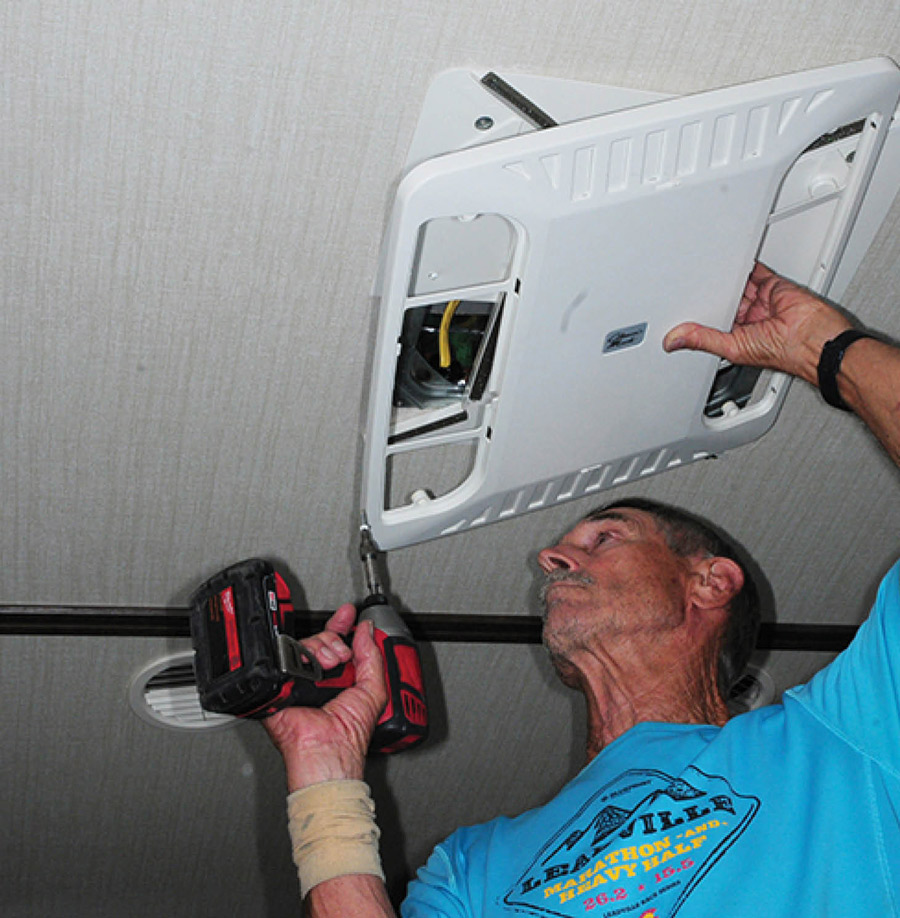 man using a drill to install an AC unit inside his RV