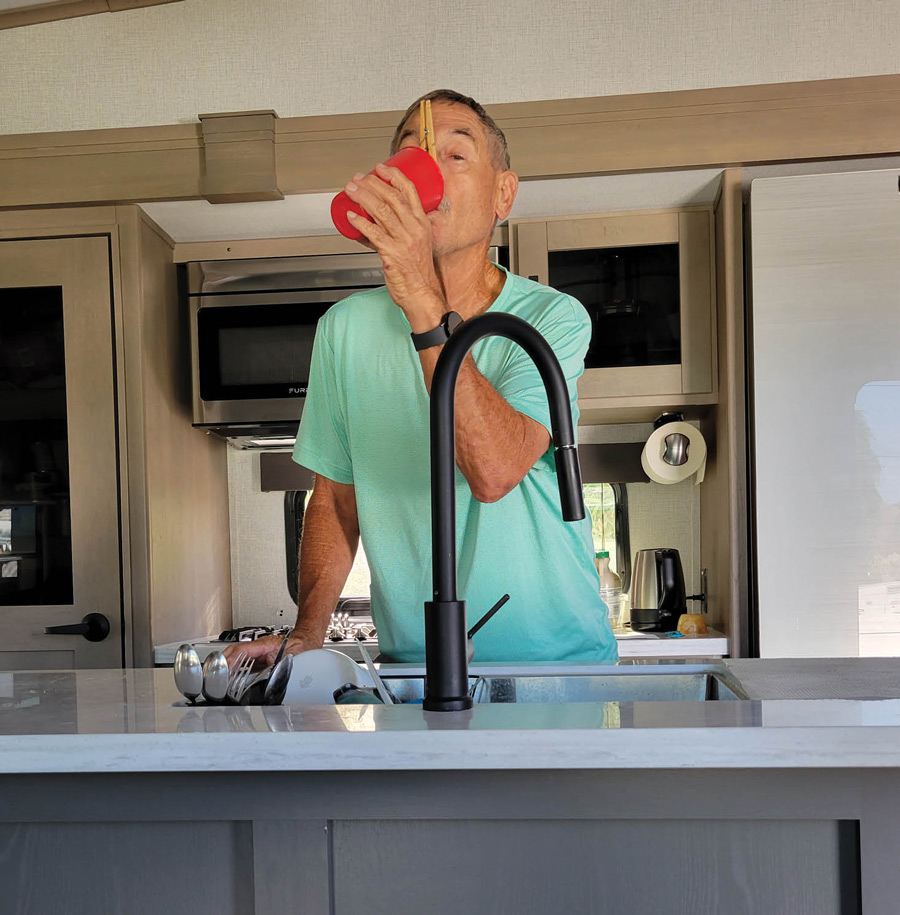 man drinking out of a cup above the sink with a clothespin on his nose