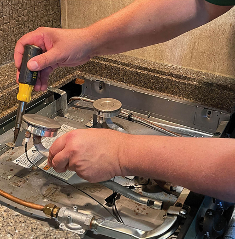 pair of hands using a screwdriver to fix a stovetop