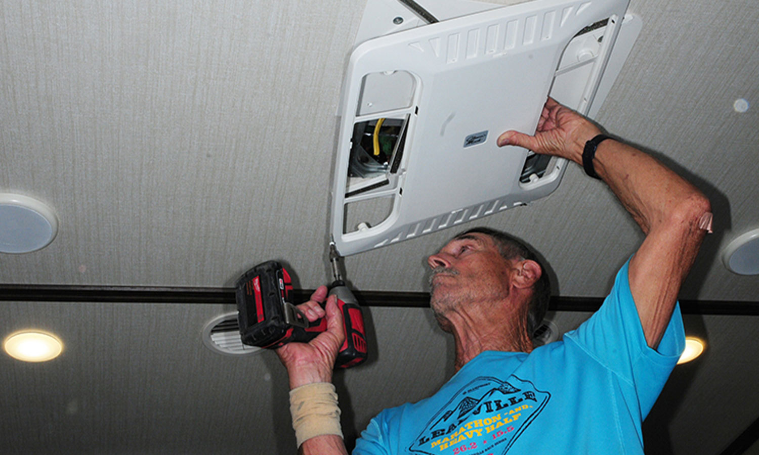 a man uses a drill gun to remove the cover vent from an RV air conditioner