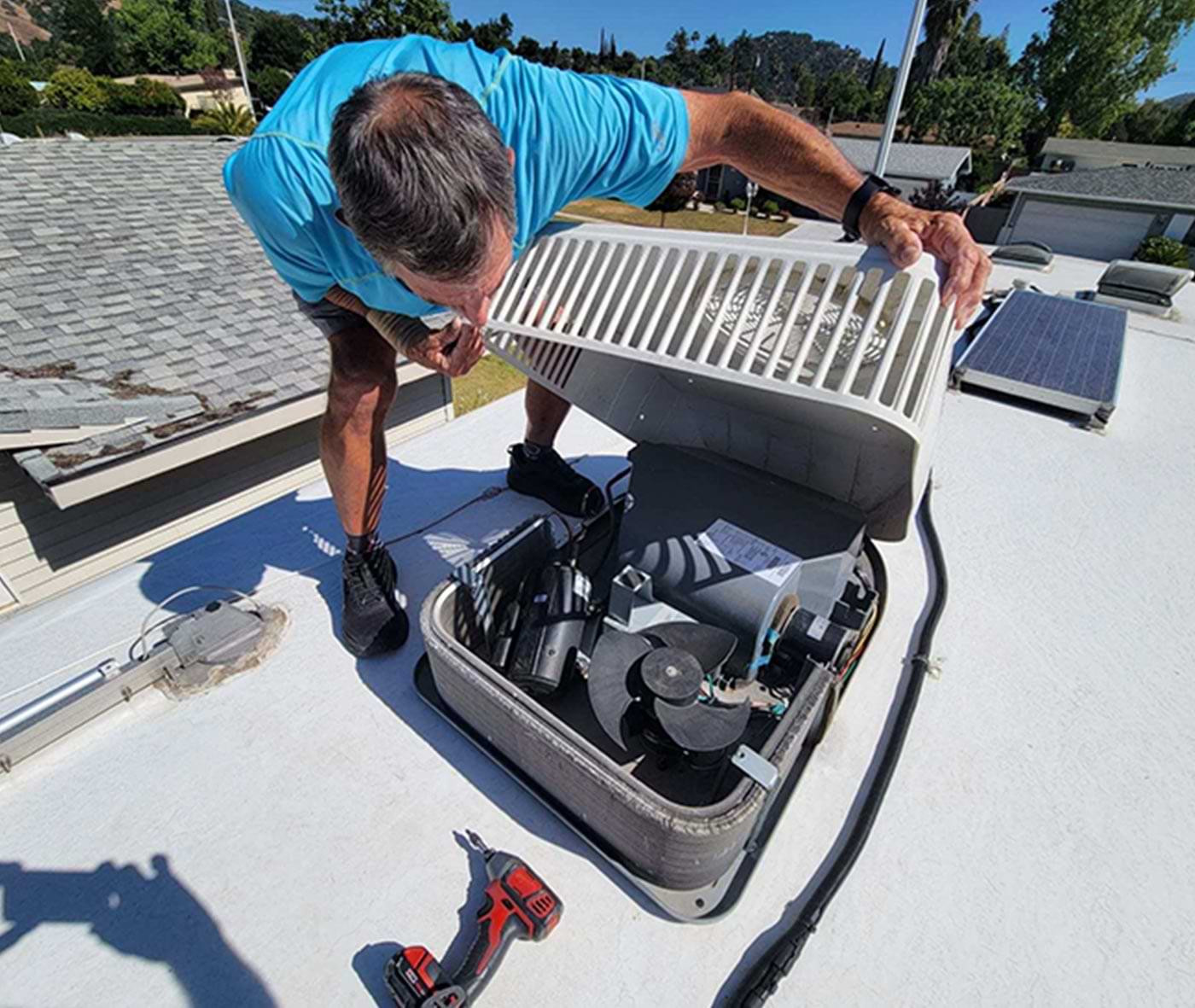 with the bolts removed a man lifts the air-conditioner shroud while standing atop the RV