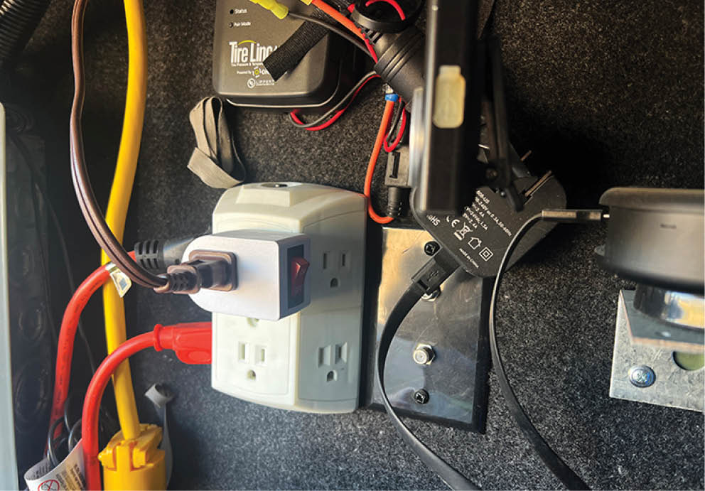 An extension cord was plugged into a lighted On/Off switch that was itself plugged into the gang adapter for the 120-volt AC outlet on the opposite wall inside the compartment. The cord was then routed closer to the chargers and cable-tied to other wiring conduit. Both chargers were plugged in at that point. This set-up provides one-switch control of power to the chargers.