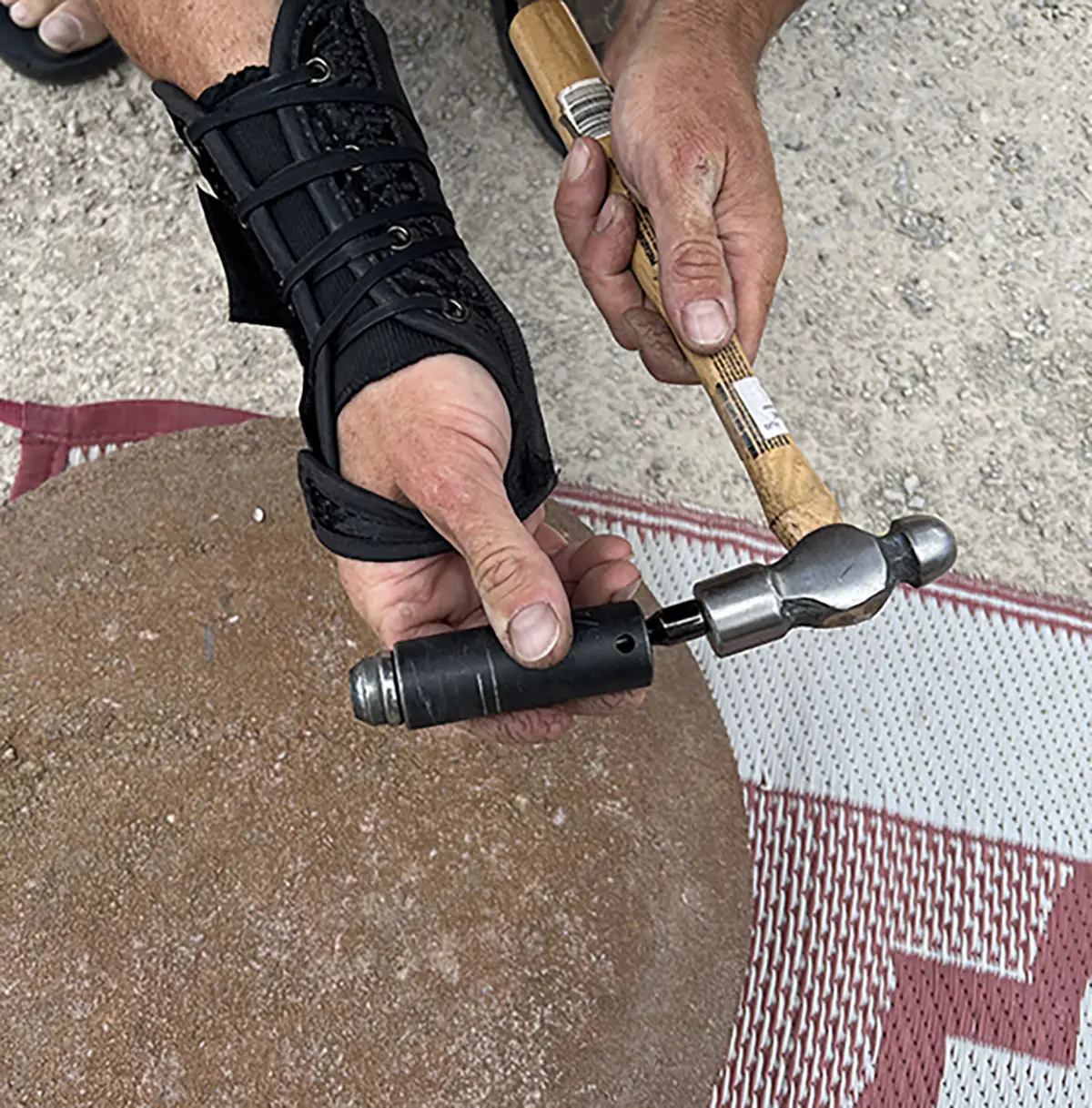 Close-up photograph perspective of a man's hand with a hammer putting it close to the half black metal original lug nut rod's socket area