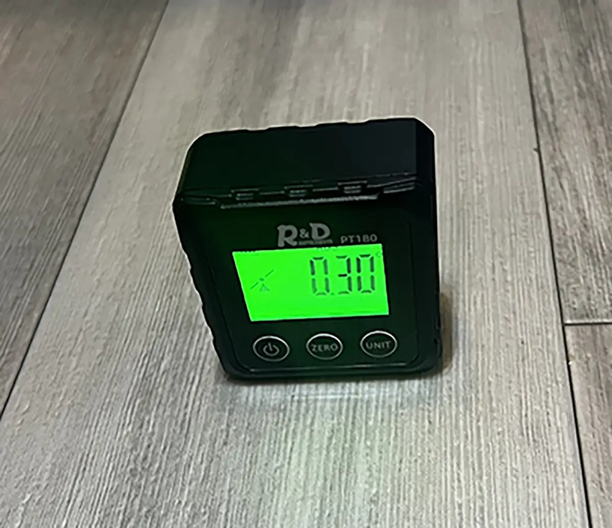 Close-up photograph perspective of the Digital Angle Finder (Digital Protractor) screen reading (in green) from R&D Instruments on a dark grey tile countertop; The reading shows 0.30 degrees and a slant tilted icon symbol