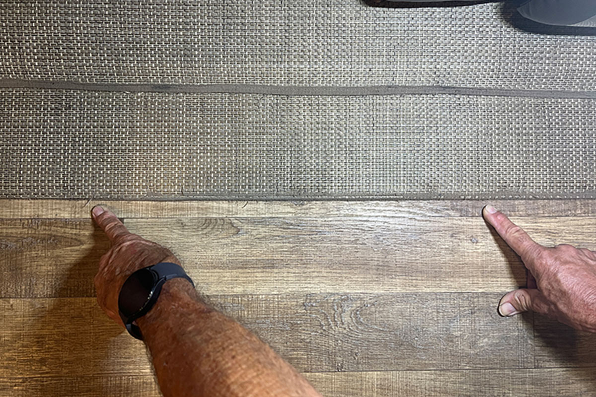 Man's hands pointing to the transition from woven vinyl flooring to vinyl plank flooring 