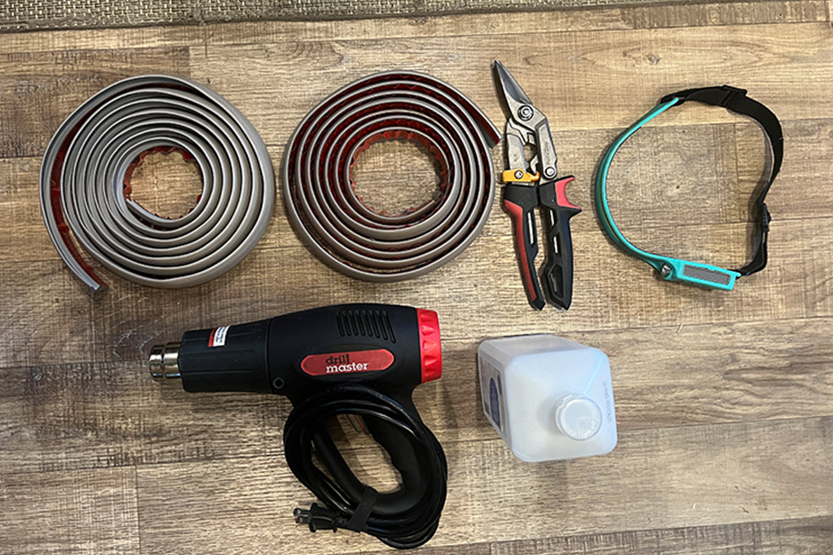 A transition strip, cutting tool, heat gun, alcohol and a headlamp sitting on the ground