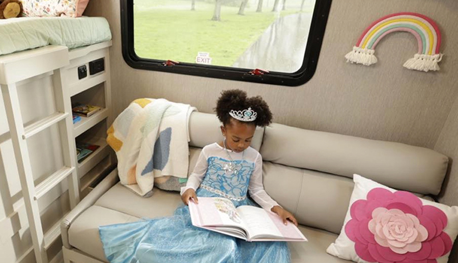 Young girl sitting on a white sofa while reading a book in REV RV Group RV