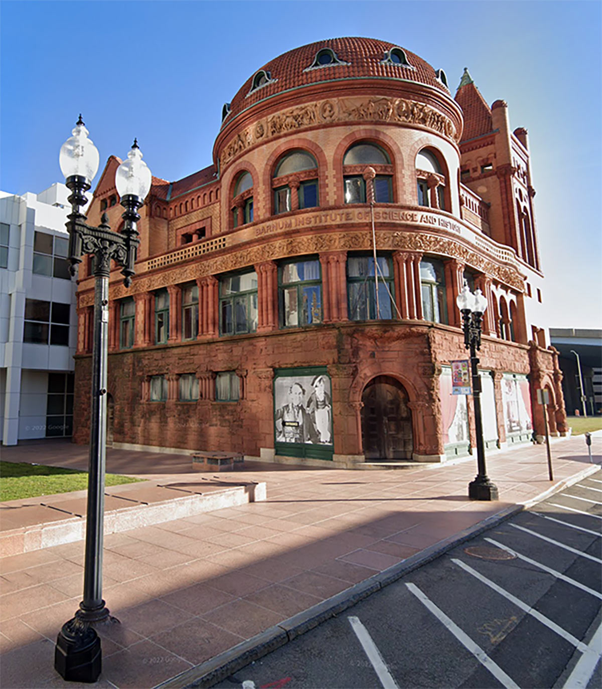 View from the street, looking up at the Barnum Institute of Science and History, a historic stone a brick building with ornate street lamps in the foreground 