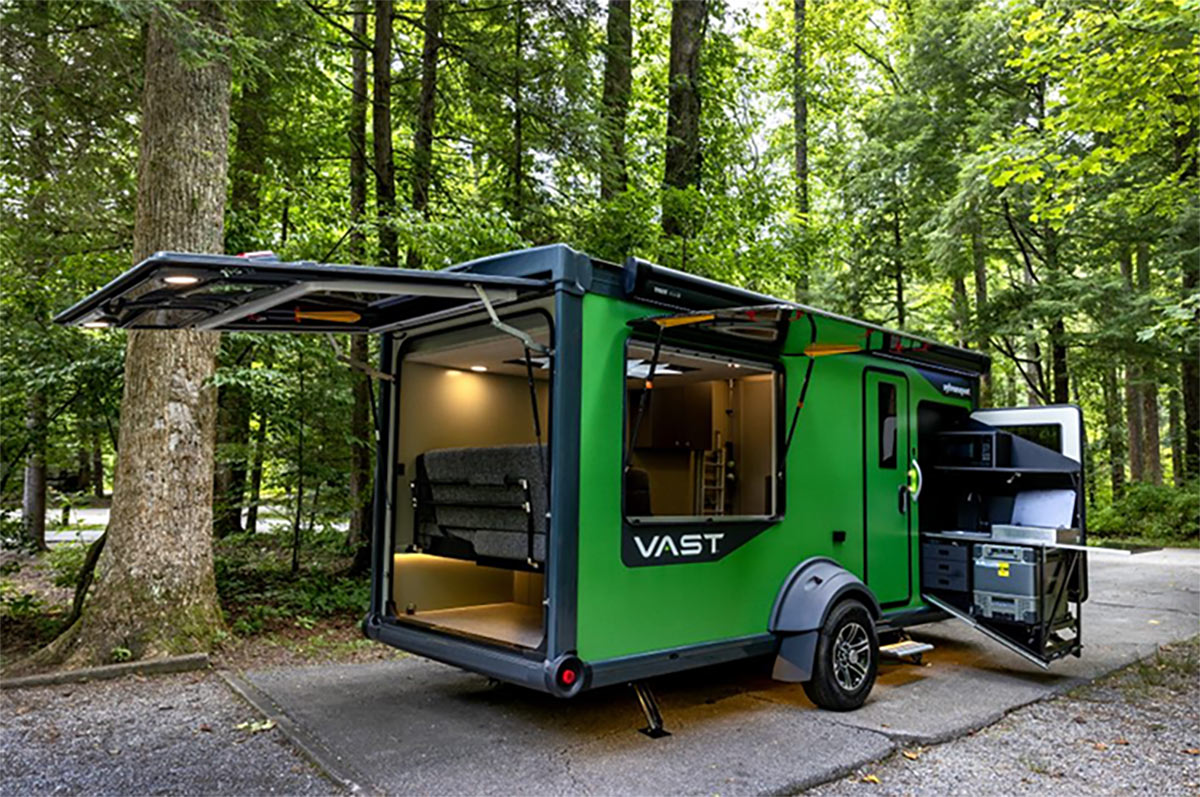 Green SylvanSport VAST adventure trailer with the back open and a side panel open, parked in the woods