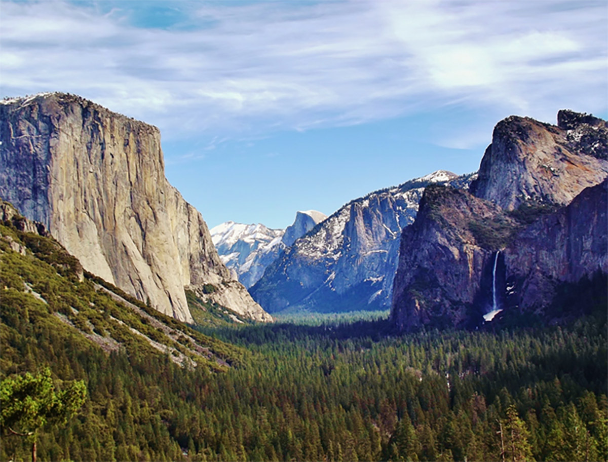 Looking down a wide valley in Yosemite National park, mountains rising out of an evergreen forest