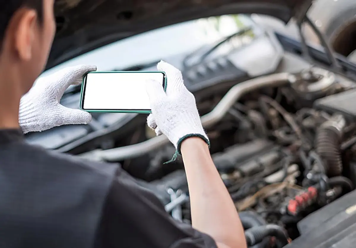 Landscape rear close-up photo view of a person holding a phone in their hands as they capture a picture of a car engine inside the fully open car hood