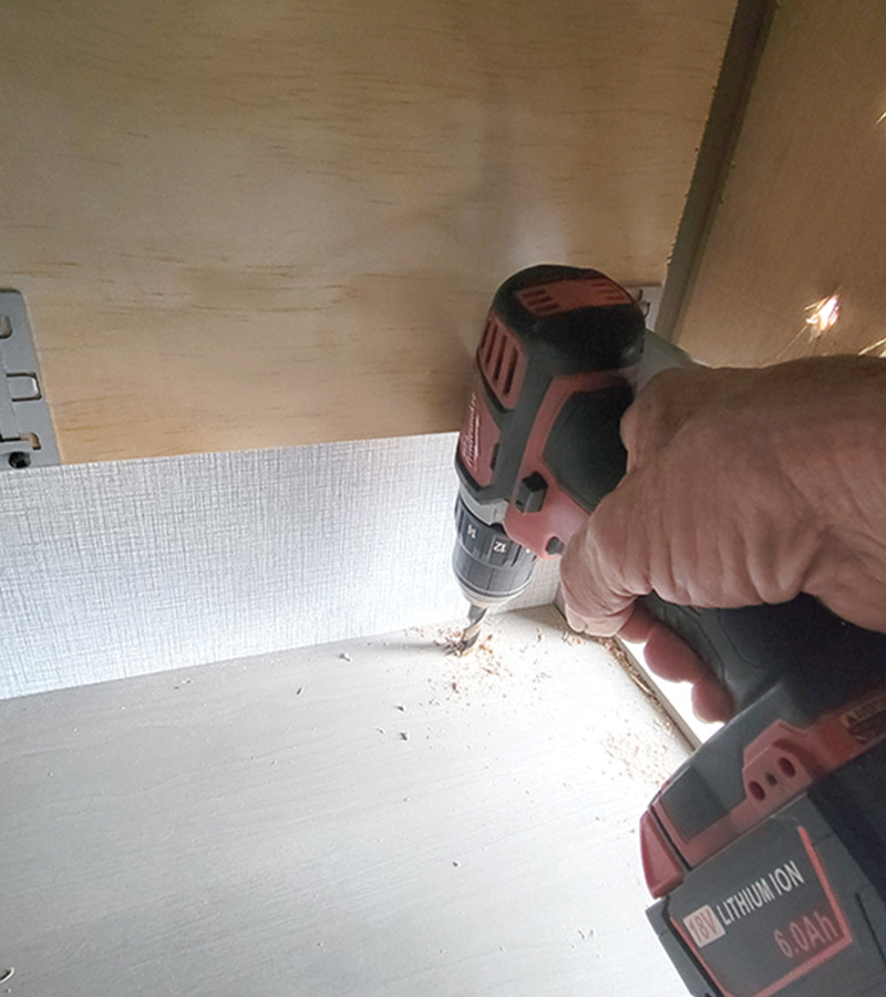 hand using drill to drill a hole in a shelf